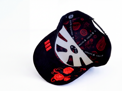 A black baseball cap with red floral embroidery on the brim, red paisley patterns on the crown, and a large white stylized 'S' logo on the front panel. The back of the cap features red embroidered details and the brand name 'SVTres' printed repeatedly.