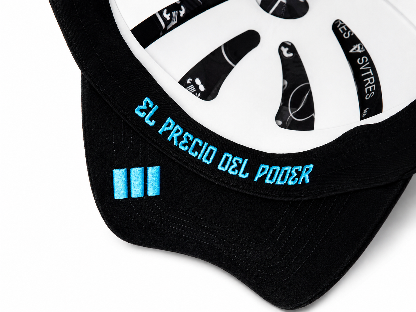 Close-up of a black and white baseball cap with bright blue embroidered text reading 'EL PRECIO DEL PODER' on the brim and three matching blue stripes on the black side panel.
